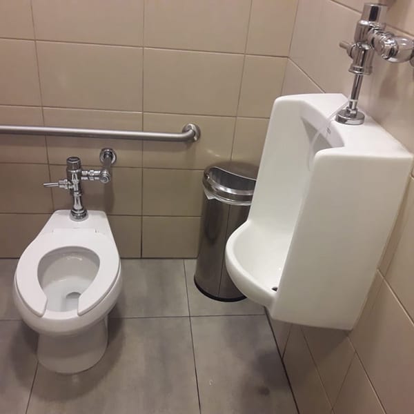 Accesorios de baño en un aseo público que incluyen inodoro y urinario con accesorios de acero inoxidable. Soluciones de fontanería y mantenimiento para instalaciones sanitarias.