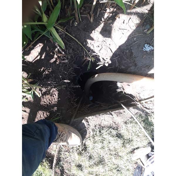 Acceso a pozo séptico con tubería de evacuación y suelo de tierra, indicando trabajos de mantenimiento y reparación de sistemas de alcantarillado.