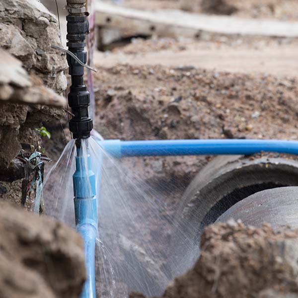 Tubería de plásticos instalada en el suelo con sistema de riego, en medio de tierra y rocas, para irrigación eficiente. Servicios técnicos especializados en instalaciones de riego y mantenimiento.